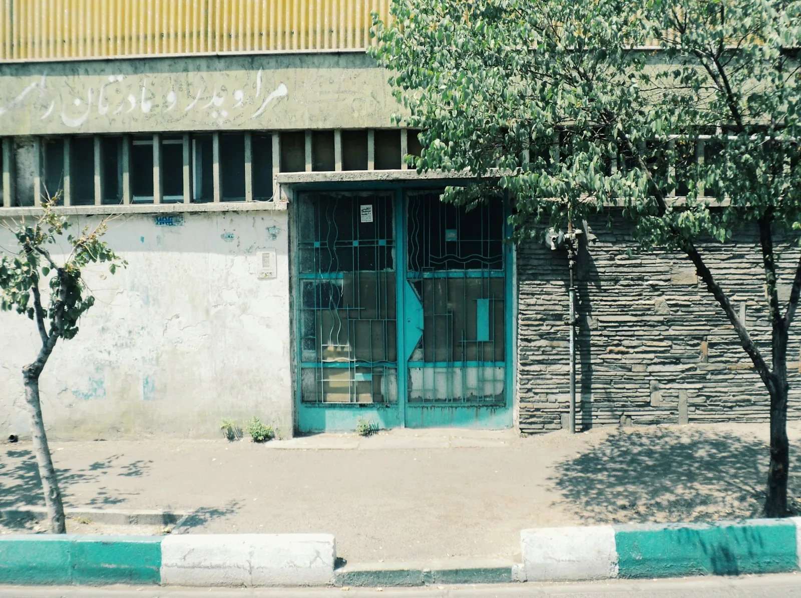 A turquoise gate between buildings and trees